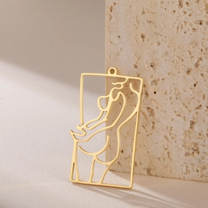 Detailed view of a gold cutout rectangle pendant with minimalist female silhouette art