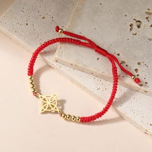 Makroansicht eines roten gewebten Armbands mit goldenem keltischem Knoten auf Stein