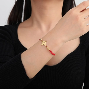 Nahaufnahme des roten Flechtarmbands mit goldenem Keltenknoten am Handgelenk