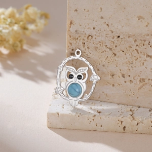 Macro detail of a silver owl pendant with blue stone on a natural beige stone backdrop