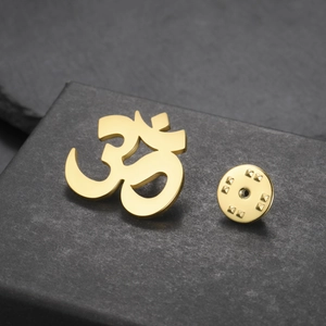 Macro detail of gold Om yoga symbol brooch with a matte finish on a stone background