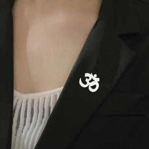 Polished silver Om yoga symbol pin attached to a black suit lapel with detailed texture