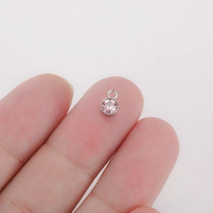 Macro shot of tiny pink birthstone charm with silver rim held on a fingertip for DIY jewelry