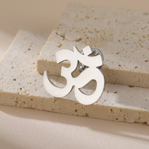 Polished stainless steel Om symbol yoga brooch pin on minimalist travertine stone display