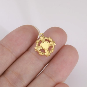 Dettaglio di un piccolo ciondolo a cuore e croce in oro tenuto in mano per la misura