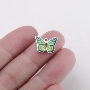 Detailed close-up of yellow and green butterfly pendant held between fingers for size