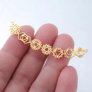 Pendentif connecteur en acier doré avec sept symboles de chakra tenu par les doigts