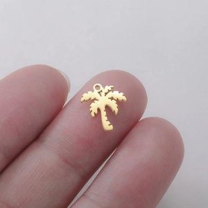 Detailed view of a small golden palm tree pendant held on a fingertip for size scale