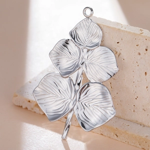Macro shot of silver leaf pendant with detailed veins on a beige stone base