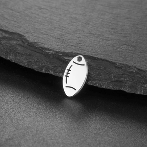 Close-up of a silver rugby ball pendant charm with textured stone background