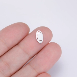 Macro detail of a silver rugby pendant held on finger to show miniature sizing