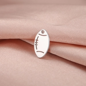 Macro shot of silver rugby ball pendant with textured finish on pink silk background