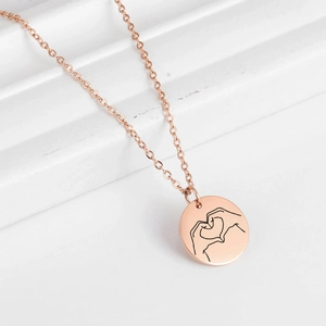 Detail of rose gold round pendant with heart gesture engraving on a cross chain necklace
