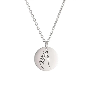 Macro detail of silver round pendant necklace with minimalist finger heart engraving