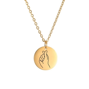 Detailed view of a golden circular pendant with a modern laser-engraved finger heart gesture