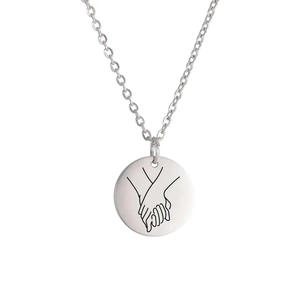 Macro detail of silver stainless steel round pendant with engraved hand-holding gesture