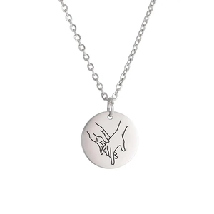 Close-up of stainless steel round pendant with laser-engraved hand-holding gesture