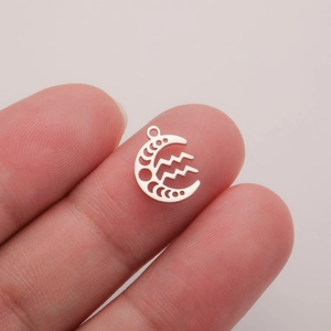 Macro view of a silver Aquarius moon pendant held between fingers to show compact size