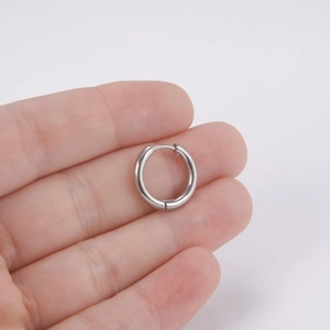 Minimalist silver polished stainless steel huggie hoop earrings held in a hand