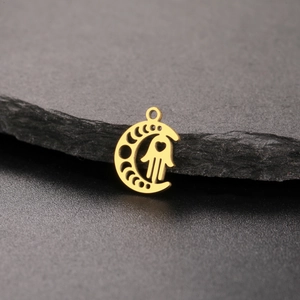 Golden crescent moon and Hamsa hand pendant with heart cutout on dark stone background
