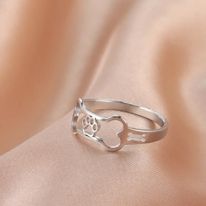 Macro view of silver hollowed-out ring featuring paw prints and bone designs on silk