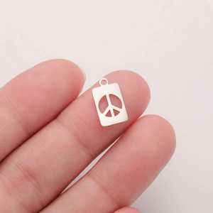 Macro shot of silver stainless steel peace sign pendant held between fingers showing size
