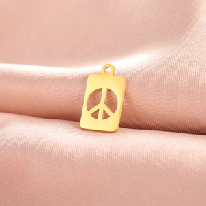 Macro shot of 18K gold plated stainless steel peace sign pendant on pink satin fabric