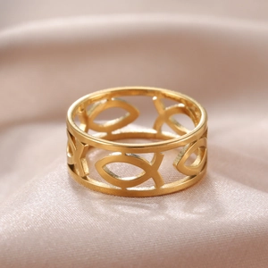 Primer plano de anillo dorado calado con patrón de peces sobre seda suave y textura de metal