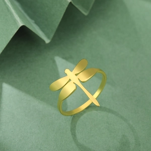 Elegante anillo de libélula en acero inoxidable dorado sobre fondo verde texturizado