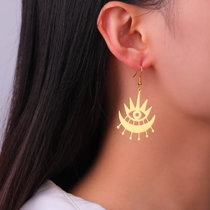 Gold hollow geometric eye and star dangle earrings on a female model with natural lighting