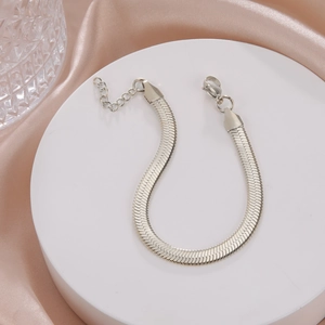 Detailed close-up of a silver flat snake chain bracelet with lobster clasp on a white stand