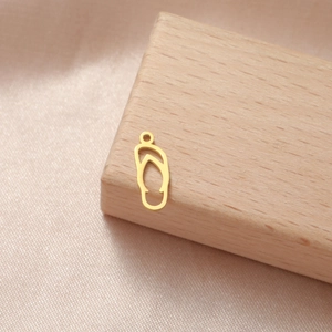 Makrodetail eines goldenen Flip-Flop-Anhängers für DIY-Schmuck auf rosa Satin-Hintergrund