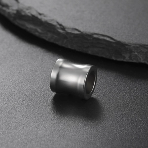 Polierte Edelstahl-Zylinderperle für DIY-Schmuck auf dunklem strukturiertem Stein