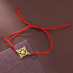 Detail of red braided cord bracelet with golden hollow geometric knot on jewelry box