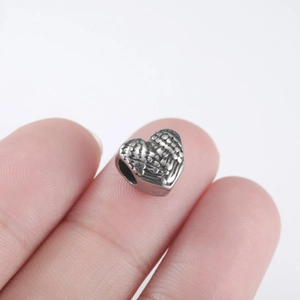 Macro detail of a vintage heart bead with wing texture held between fingers for size reference
