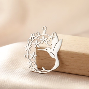 Détail d'un pendentif colibri argenté avec fleurs sur un fond de satin élégant