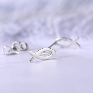 Macro shot of silver minimalist fish stud earrings on purple textured fabric background