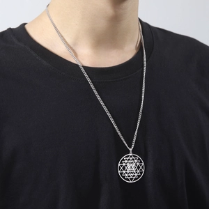 Detail van de zilveren geometrische ketting met ronde hanger op een zwart shirt