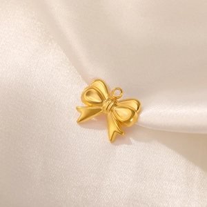 Detailed macro view of a golden bow-shaped stainless steel pendant on white satin fabric