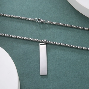 Detalle del collar con colgante de barra de acero inoxidable plateado y cadena box sobre verde