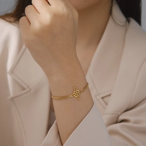 Gros plan sur pendentif nœud celtique doré et chaîne à billes sur poignet avec blazer beige