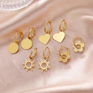 Four pairs of golden stainless steel heart and sunburst charm huggie earrings on silk
