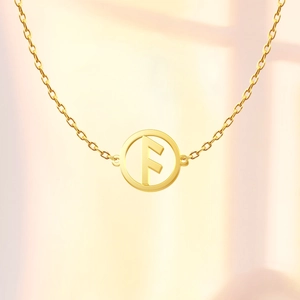 Detail shot of a gold Viking rune pendant with an engraved F symbol on a delicate O-chain