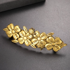 Vintage gold floral hair clip with four flowers and insects on a dark textured background