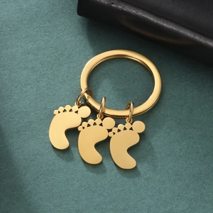Golden stainless steel keychain with three baby feet pendants on a textured background