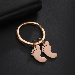 Detailed close-up of rose gold baby feet pendants on a polished steel keychain ring