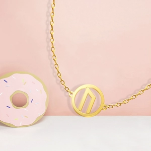 Detail of 18K gold-plated Viking Rune pendant necklace on a decorative pink background