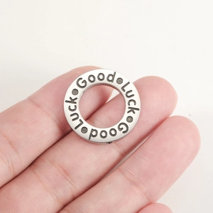 Polished stainless steel round pendant with Good Luck engraving held by fingers