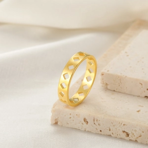 Primer plano de un anillo de acero dorado con rombos huecos sobre base de mármol beige