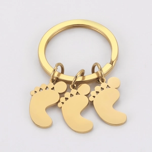 Close-up of three polished gold baby feet charms on a stainless steel keychain ring